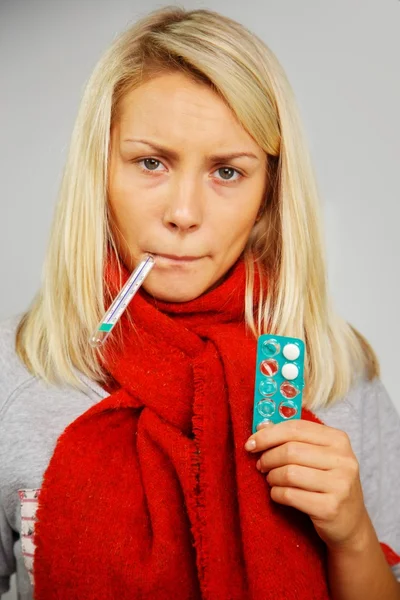 Mujer rubia joven enferma con pastillas y termómetro — Foto de Stock