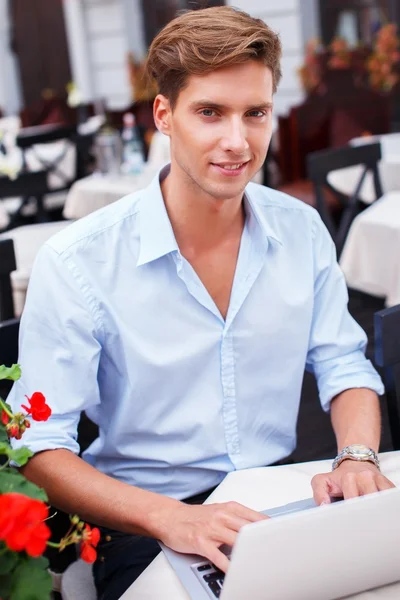 Knappe jonge man met laptop in een zomerterras — Stockfoto