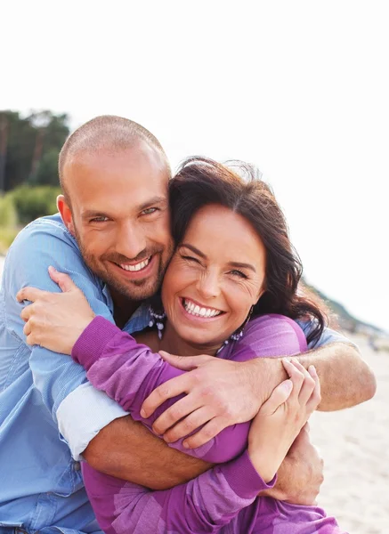 Joyeux couple souriant d'âge moyen sur une plage — Photo