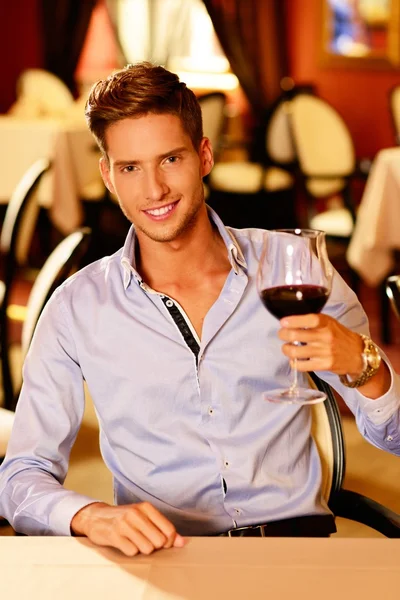 Schöner junger Mann mit einem Glas Rotwein im Restaurant — Stockfoto