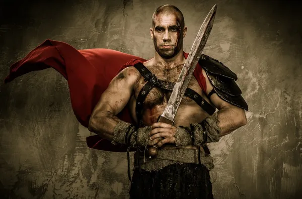 Wounded gladiator in waving coat holding sword covered in blood — Stock Photo, Image