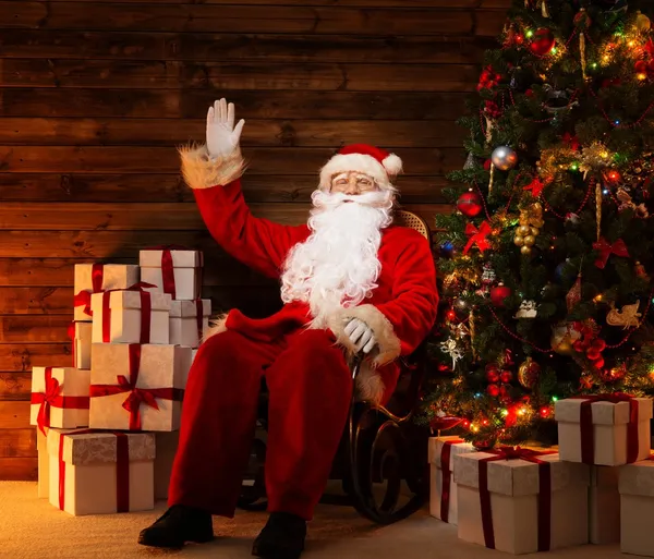 圣诞老人坐在摇椅里木居家室内与他周围的礼品盒 — 图库照片