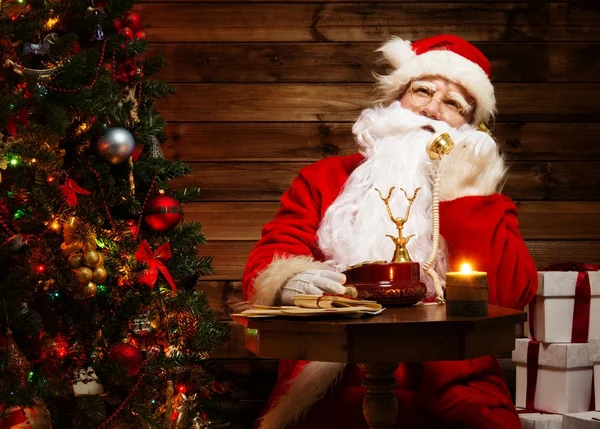 Papai Noel falando por telefone no interior da casa de madeira — Fotografia de Stock