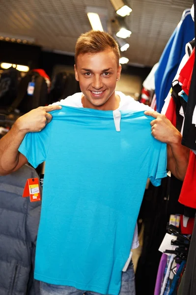 Joven guapo eligiendo camiseta en un outlet deportivo —  Fotos de Stock