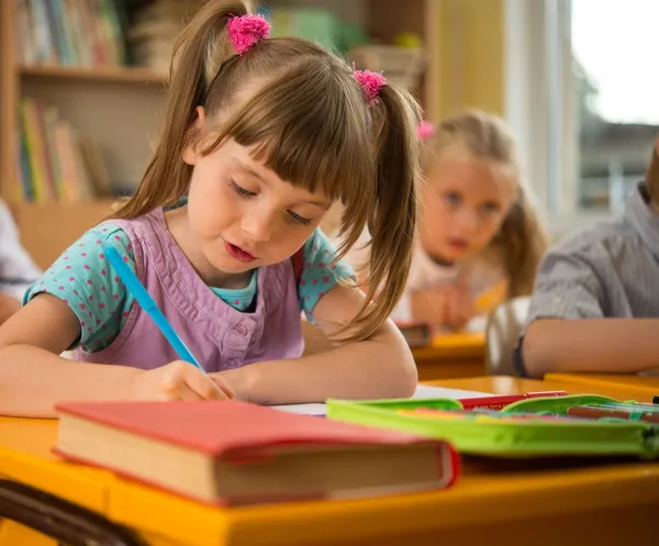 Piccola studentessa seduta dietro la scrivania della scuola durante la lezione a scuola — Foto Stock