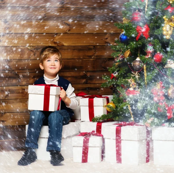 Little boy with gift box under christmas tree in wooden house interior