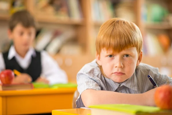 Kleiner rothaariger Schüler während des Unterrichts hinter der Schulbank — Stockfoto