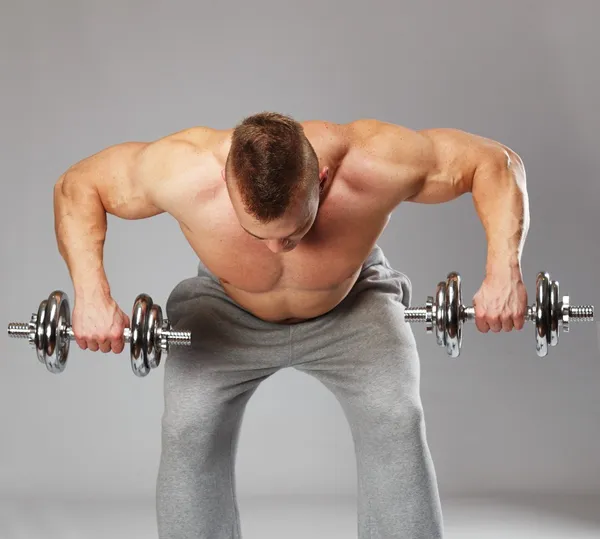 Guapo joven musculoso haciendo ejercicio con mancuernas — Foto de Stock