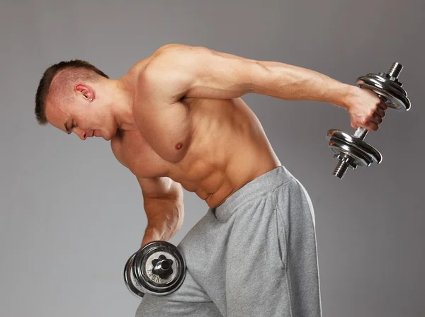 Guapo joven musculoso haciendo ejercicio con mancuernas —  Fotos de Stock