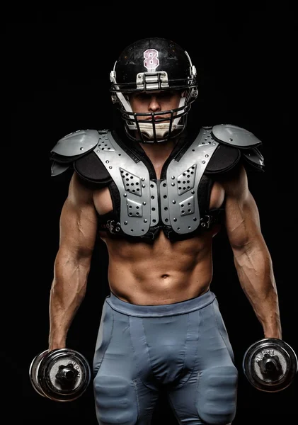 American football player with dumbbells wearing helmet and protective armour — Stock Photo, Image