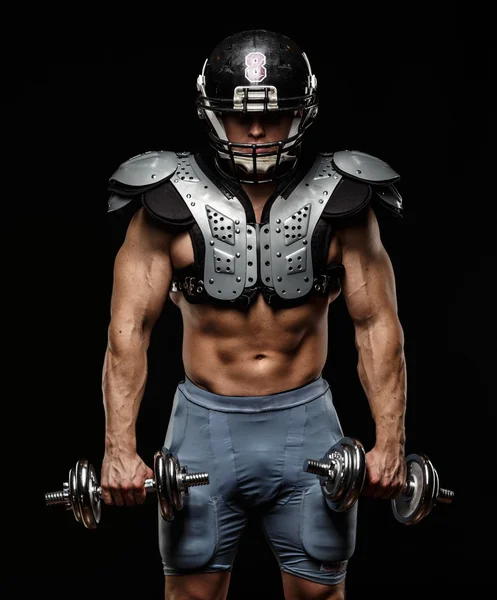 American football player with dumbbells wearing helmet and protective armour — Stock Photo, Image