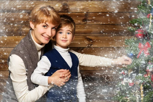 Glückliche Mutter und ihr kleiner Junge schmücken Weihnachtsbaum im Holzhaus-Interieur — Stockfoto