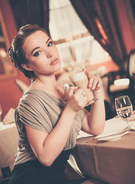 Schönes junges Mädchen mit einer Tasse Kaffee allein in einem Restaurant — Stockfoto