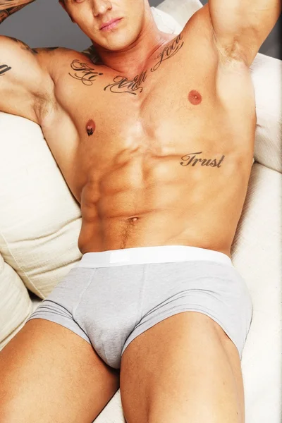 Man with beautiful muscular tattooed torso in underwear lying on sofa — Stock Photo, Image