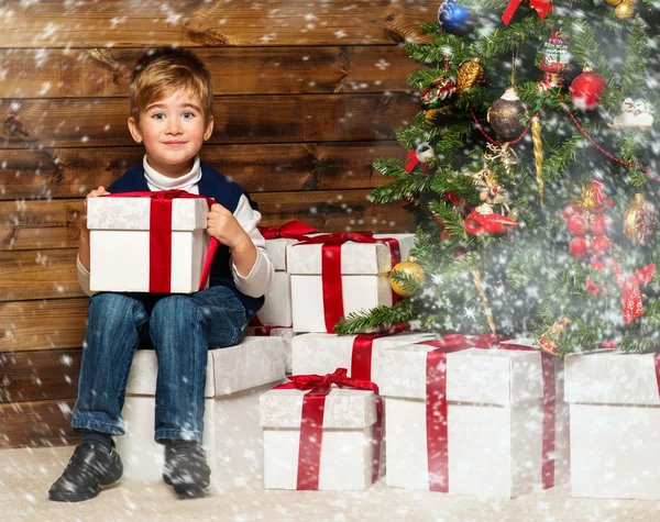 Kleiner Junge mit Geschenkbox unter dem Weihnachtsbaum im Holzhaus-Interieur — Stockfoto