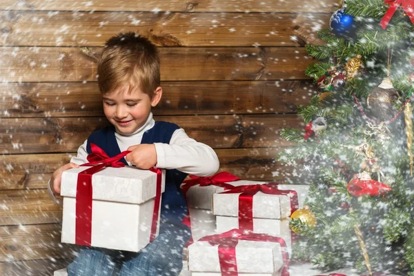 Little boy opening gift box under christmas tree in wooden house interior — Stock Photo, Image