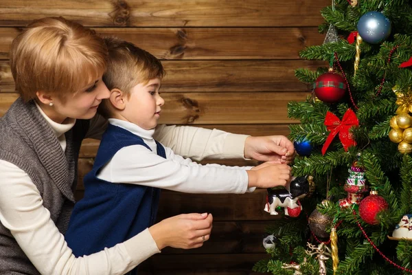 Glad mamma och sin lilla pojke dekorera julgran i trähus inre — Stockfoto