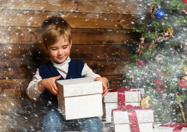 Μικρό αγόρι άνοιγμα δώρο κουτί κάτω από το χριστουγεννιάτικο δέντρο στο εσωτερικό ξύλινο σπίτι — Φωτογραφία Αρχείου