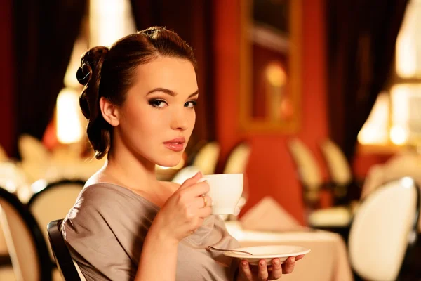 Красивая молодая девушка с чашкой кофе в одиночестве в ресторане — стоковое фото