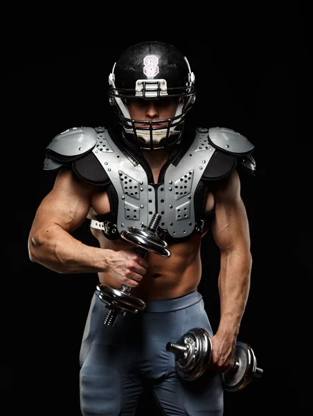 American football player with dumbbells wearing helmet and protective armour — Stock Photo, Image