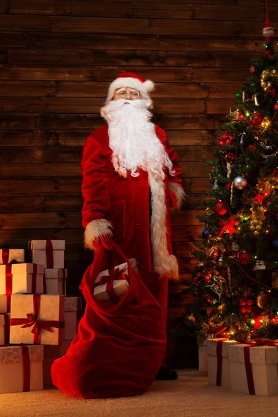 Santa claus v dřevěných domů interiéru s pytlem plným vánoční dárky — Stock fotografie