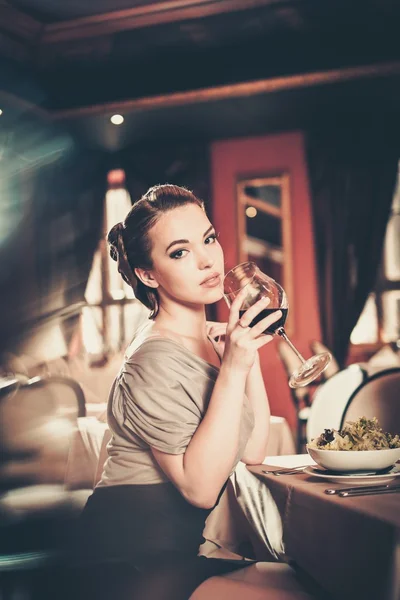 Vacker ung flicka med glas rödvin ensam i en restaurang — Stockfoto