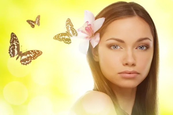 Mooie jonge brunette vrouw met orchideebloem in haar haren en vlinders — Stockfoto