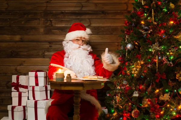 Père Noël à l'intérieur de la maison en bois assis derrière la table et écrivant des lettres avec plume — Photo