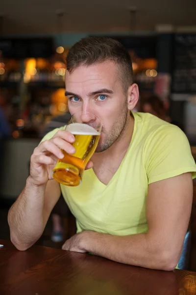 Schöner junger Mann trinkt leichtes Bier in einer Kneipe — Stockfoto