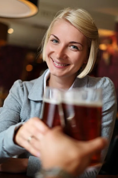 Young woman with beer toasting in a pub — Stock Photo, Image