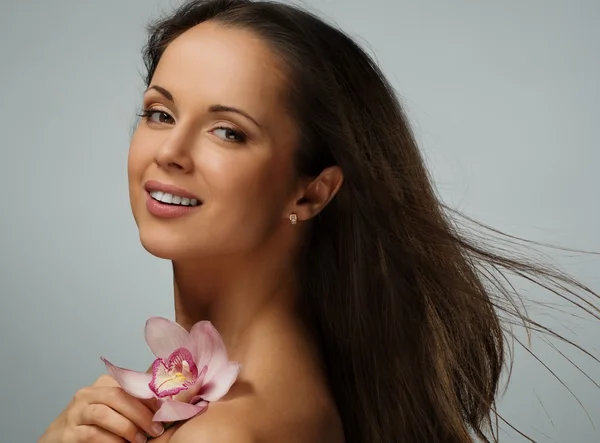 Junge schöne brünette Frau mit wehendem Haar und Orchideenblume — Stockfoto