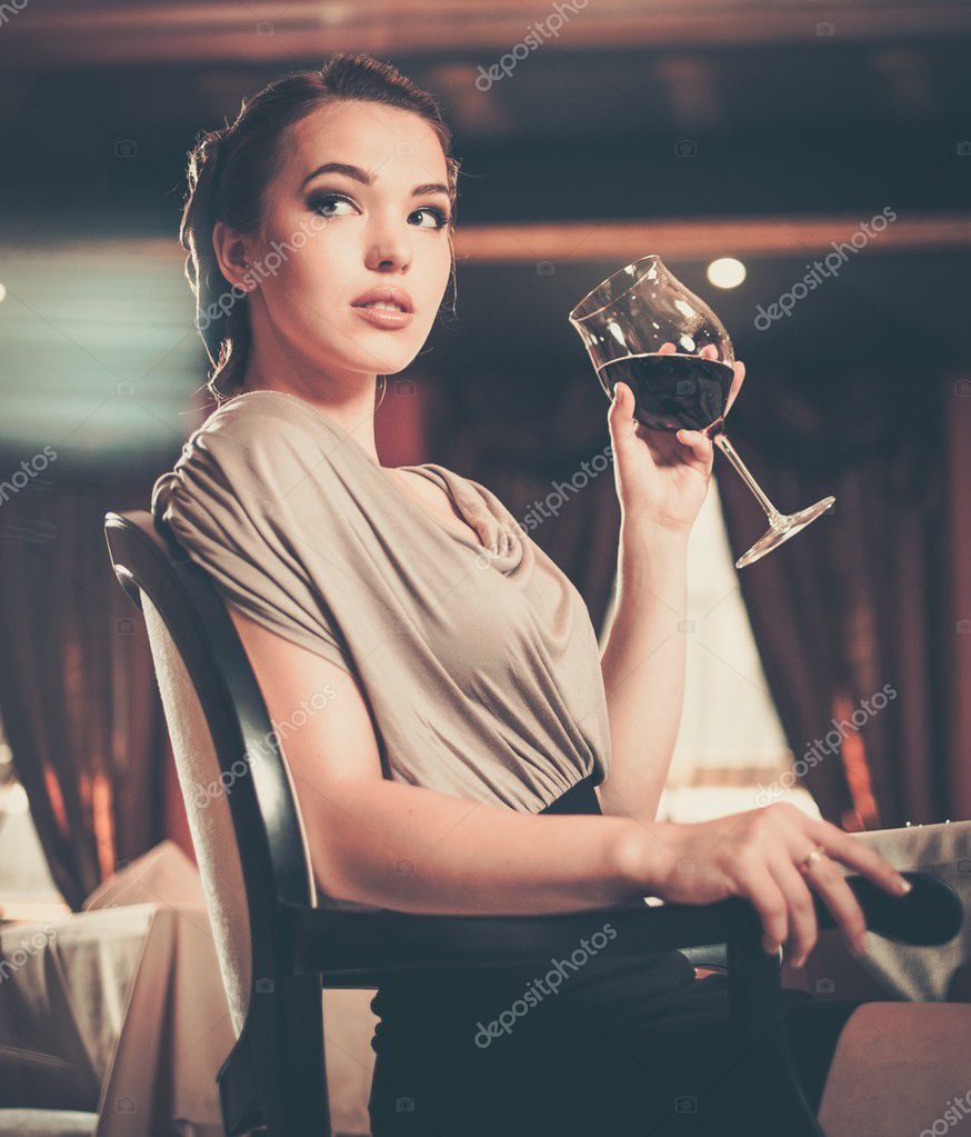 Beautiful young girl with glass of red wine alone in a restaurant
