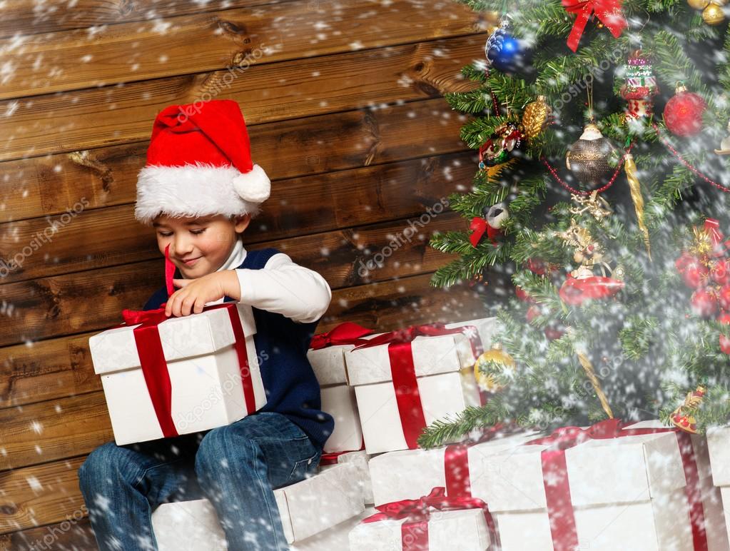 Little boy opening gift box under christmas tree in wooden house