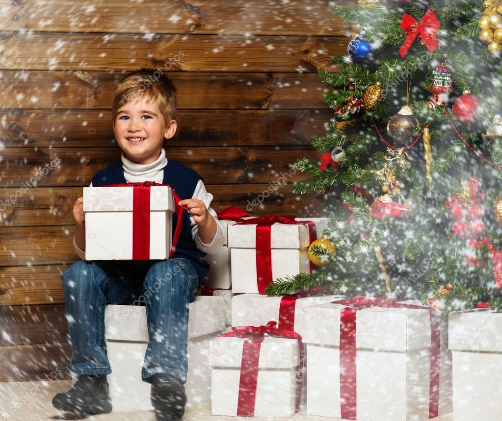 Little boy with gift box under christmas tree in wooden house interior