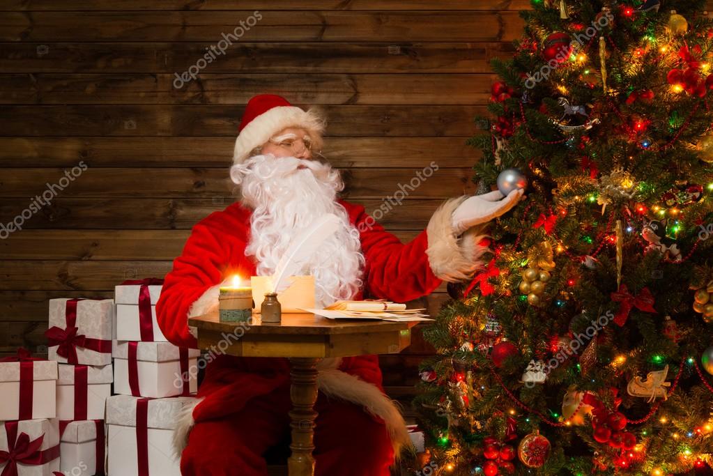 Papai Noel em casa de madeira interior olhando para árvore de Natal  decorada fotos, imagens de © nejron #36577705