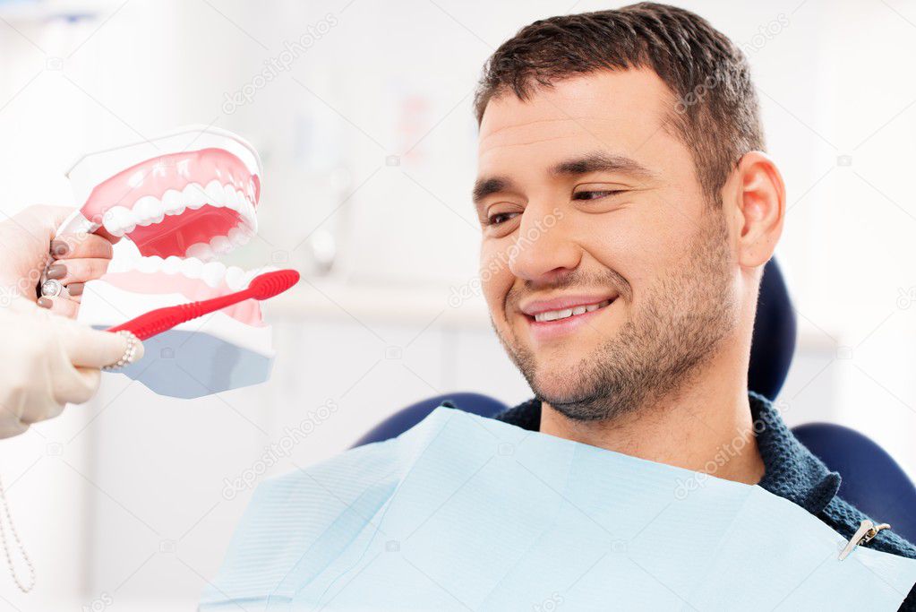 Dentist showing to man patient on mockup how to clean teeth Stock Photo