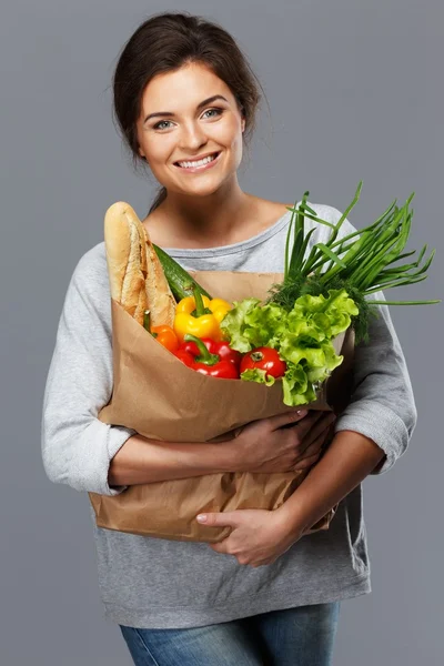 Усміхнена молода брюнетка з продуктовою сумкою, повна свіжих овочів — стокове фото