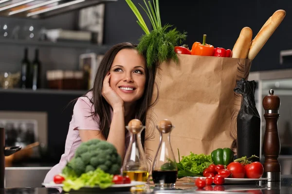 Mujer joven con bolsa de supermercado llena de verduras frescas en una cocina moderna — Foto de Stock