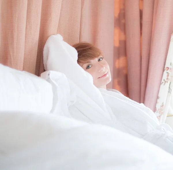 Hermosa mujer en albornoz con un corte de pelo corto acostado en una cama — Foto de Stock