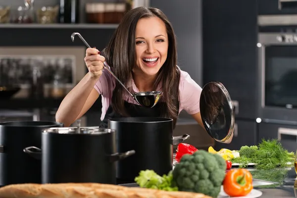 Joven alegre en delantal en la cocina moderna saboreará cucharón de olla — Foto de Stock