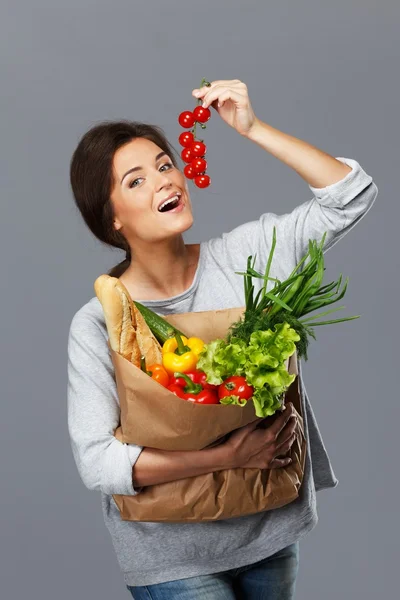 Smiling brunette woman with grocery bag full of fresh vegetables and cherry tomatoes — Stock Photo, Image