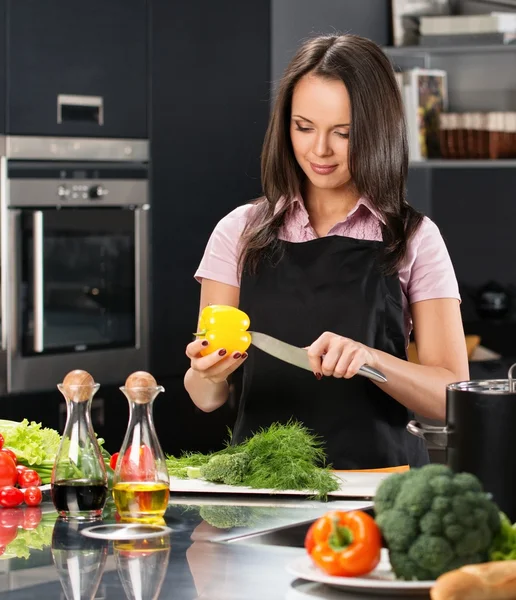 Glad ung kvinna i förkläde på modernt kök skära grönsaker — Stockfoto