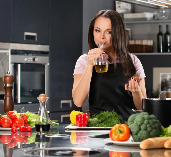 Jonge vrouw in schort op moderne keuken ruiken olijfolie — Stockfoto