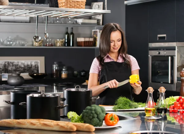 Vrolijke jonge vrouw in schort op moderne keuken snijden groenten — Stockfoto