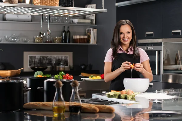 Jonge vrouw in schort breken van eieren voor een deeg op een moderne keuken — Stockfoto