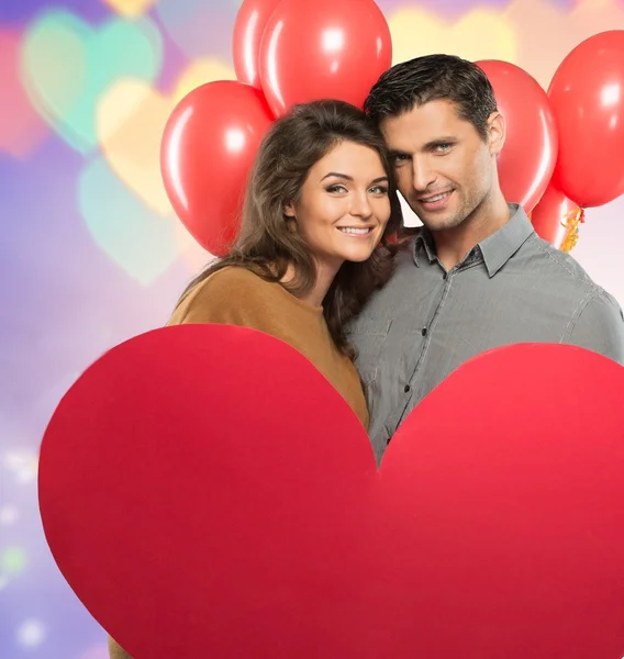 Feliz pareja sosteniendo el corazón de papel hecho a mano y globos rojos sobre fondo bokeh — Foto de Stock