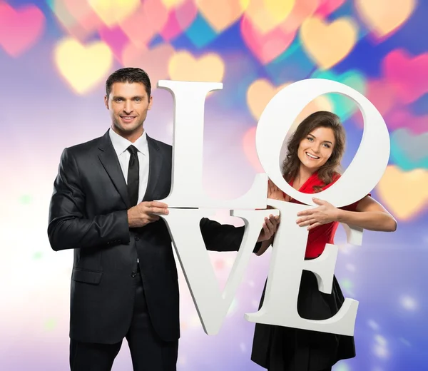 Beautiful smiling couple holding word LOVE over bokeh background — Stock Photo, Image