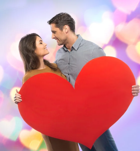 Happy couple in shirt and dress holding handmade paper heart over blurred background — Stock Photo, Image