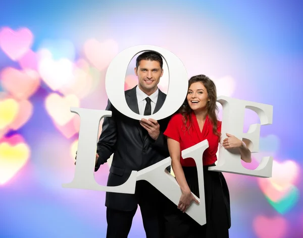Schöne lächelnde Paar hält Wort Liebe über Bokeh Hintergrund — Stockfoto