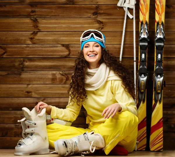 Glückliche Frau mit Skiern und Skischuhen, die auf einem Fußboden neben einer Holzwand sitzt — Stockfoto